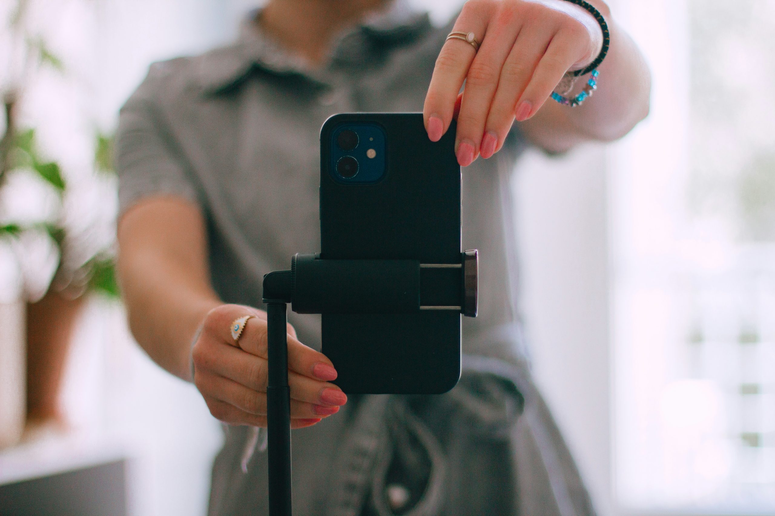 a woman in a grey dress is positioning a mobile phone on a stand before starting filming.