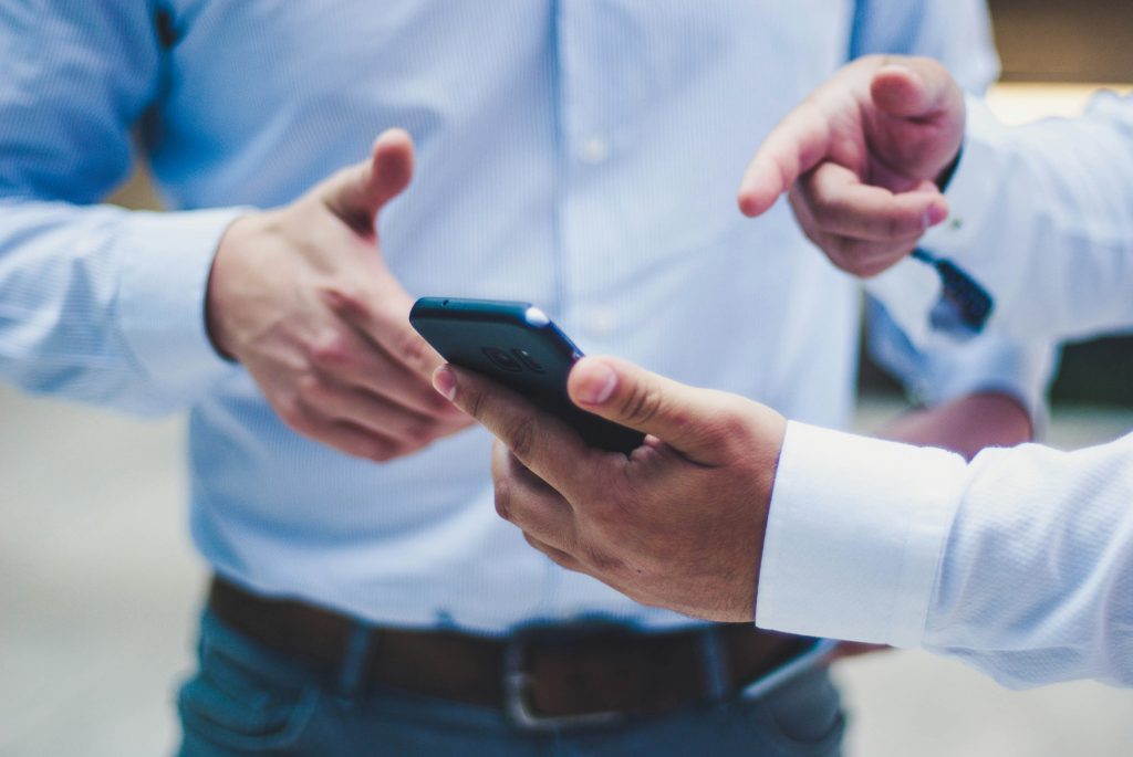 two men in blue suit shirts are looking at a mobile phone.